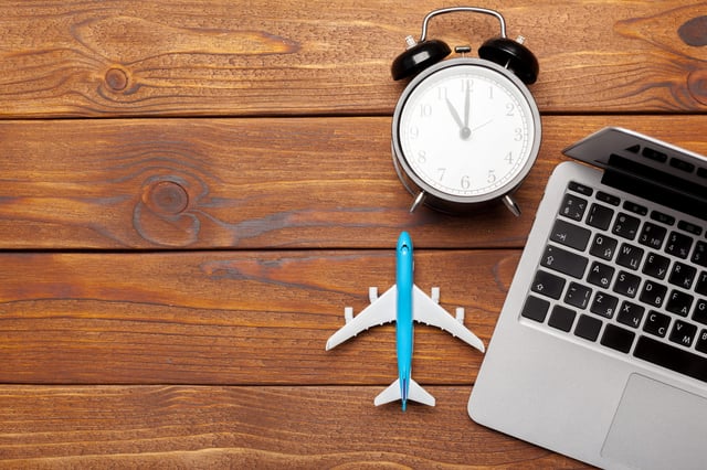 A clock, a laptop and an aeroplane toy on a wooden table