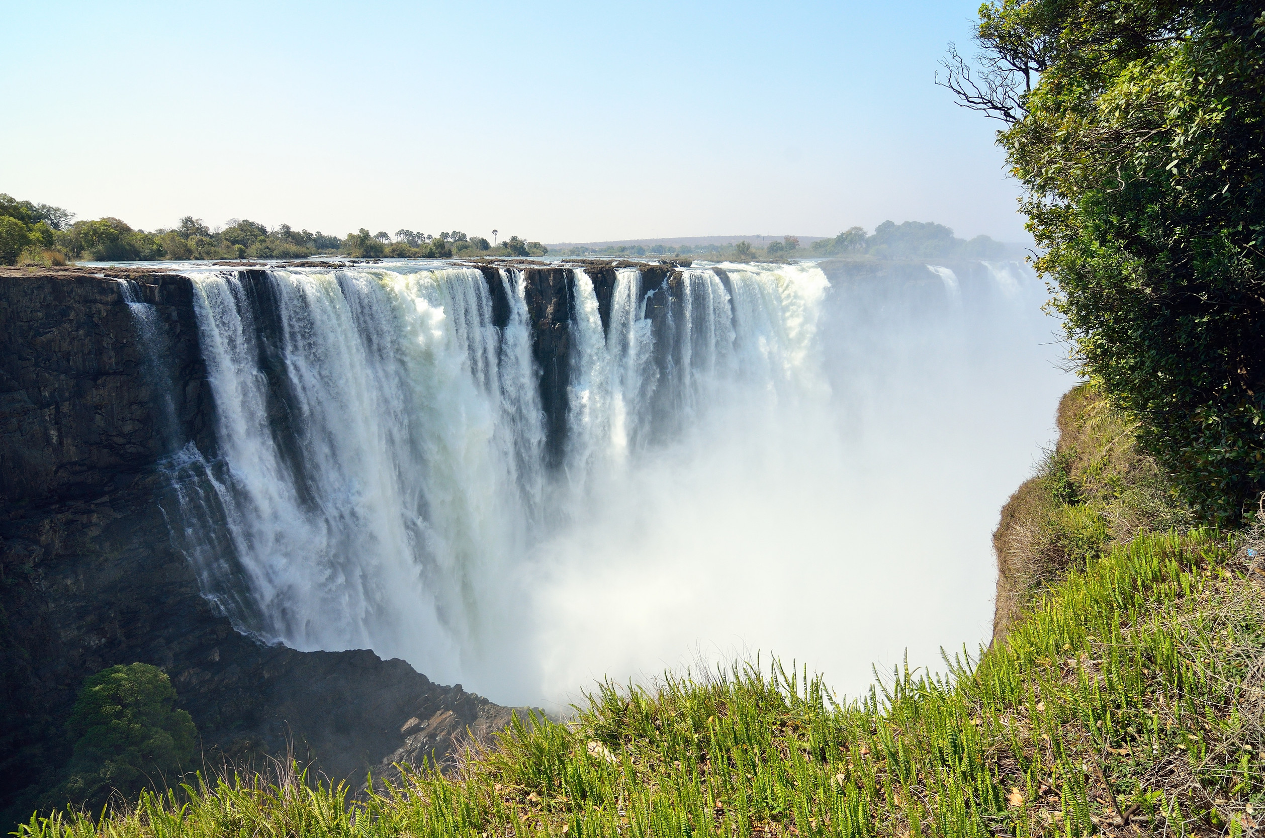 The thundering roar of Victoria Falls fills the air as water crashes down a vast cliff face, creating a mesmerizing curtain of mist